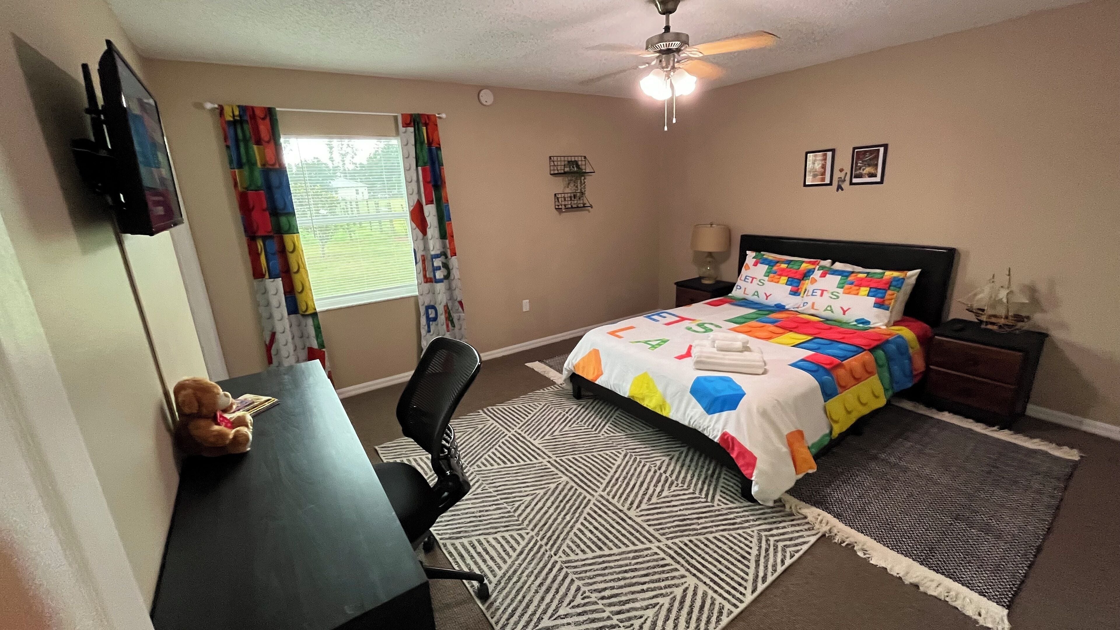 Een slaapkamer met een bed, bureau, stoel en een raam met gordijnen.