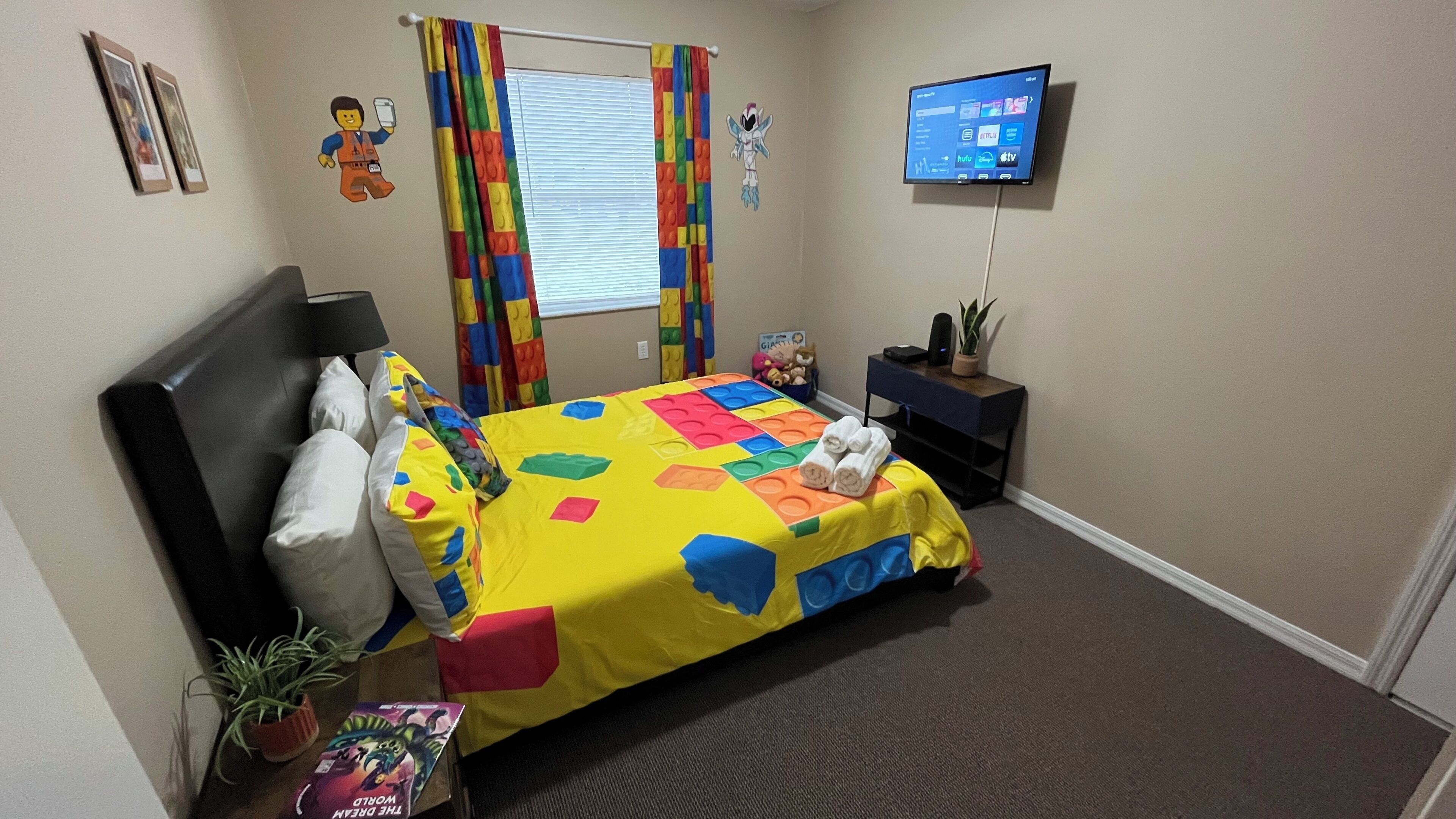 Quarto com cama, televisão, escrivaninha e janela com cortinas.