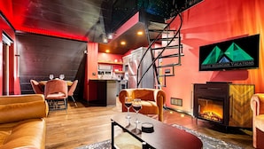 A modern interior with a fireplace, seating area, and a kitchen in the background. - Luxury Adults-Only A-Frames |Table Rock (Omaha)