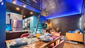 A modern kitchen with stainless steel appliances, a dining area with a wooden table set for four, and a cozy seating area with a sofa and armchairs. - Luxury Adults-Only A-Frames |Table Rock (Omaha)