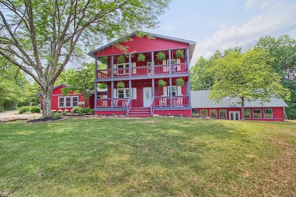 A two-story red building with a balcony on the upper floor, surrounded by a well-maintained lawn and trees.