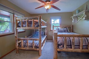 A room with two bunk beds made of wood, a ceiling fan, and a window with blinds.