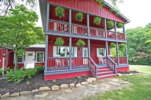 A two-story house with a red exterior, a balcony on each floor, and a front porch with steps leading to the entrance.