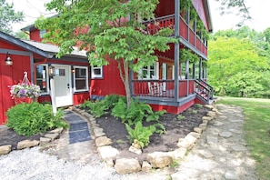 A red multi-story house with a front porch, a stone pathway, and a small garden area.