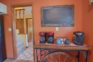 A hallway with a staircase, a coffee station with two coffee makers, a mug, and a kettle.