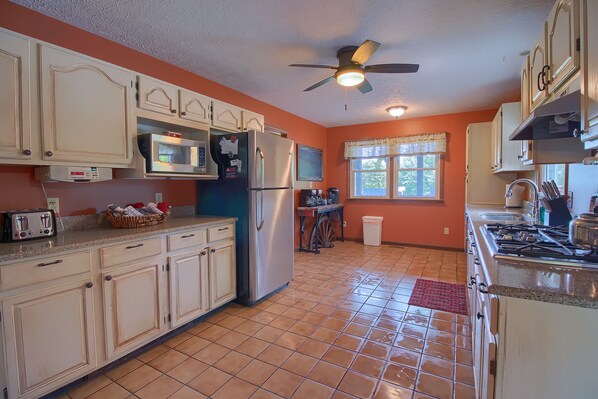 A kitchen with white cabinets, a microwave, a refrigerator, a stove, and a ceiling fan.