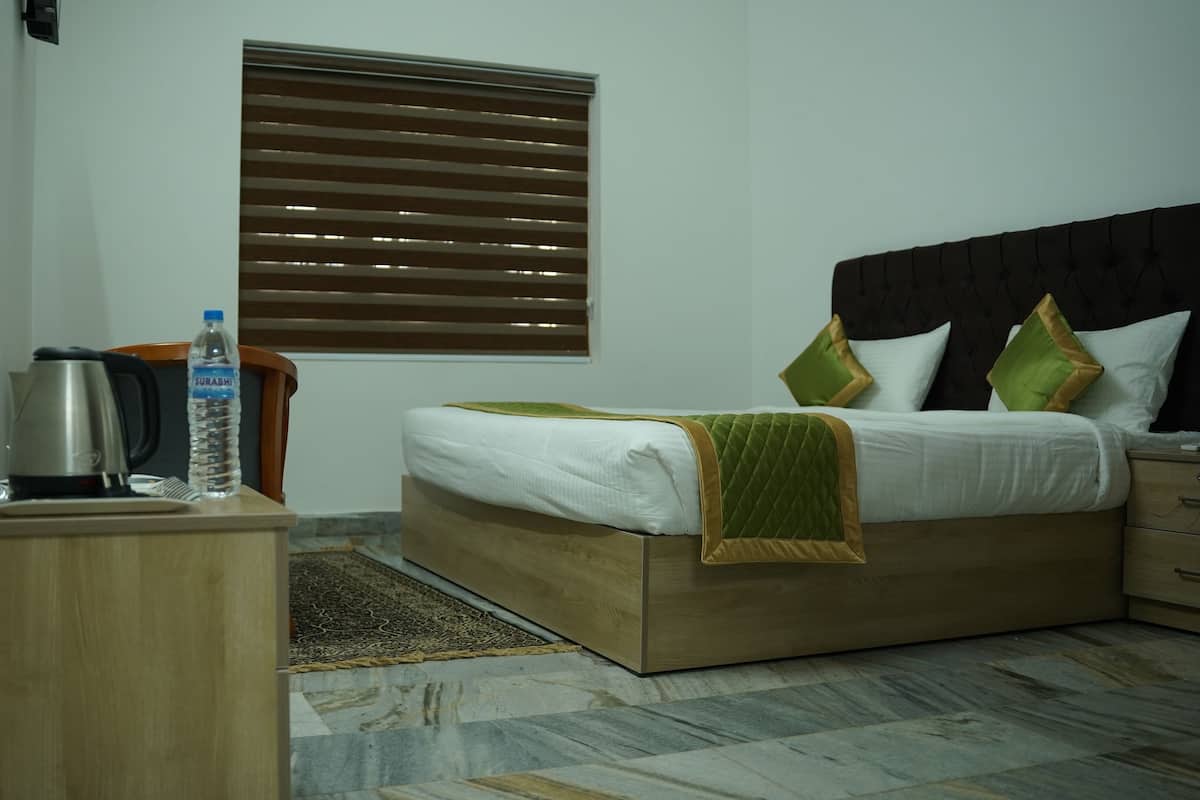 Quarto de hotel com cama, mesa de cabeceira e janela com persianas.