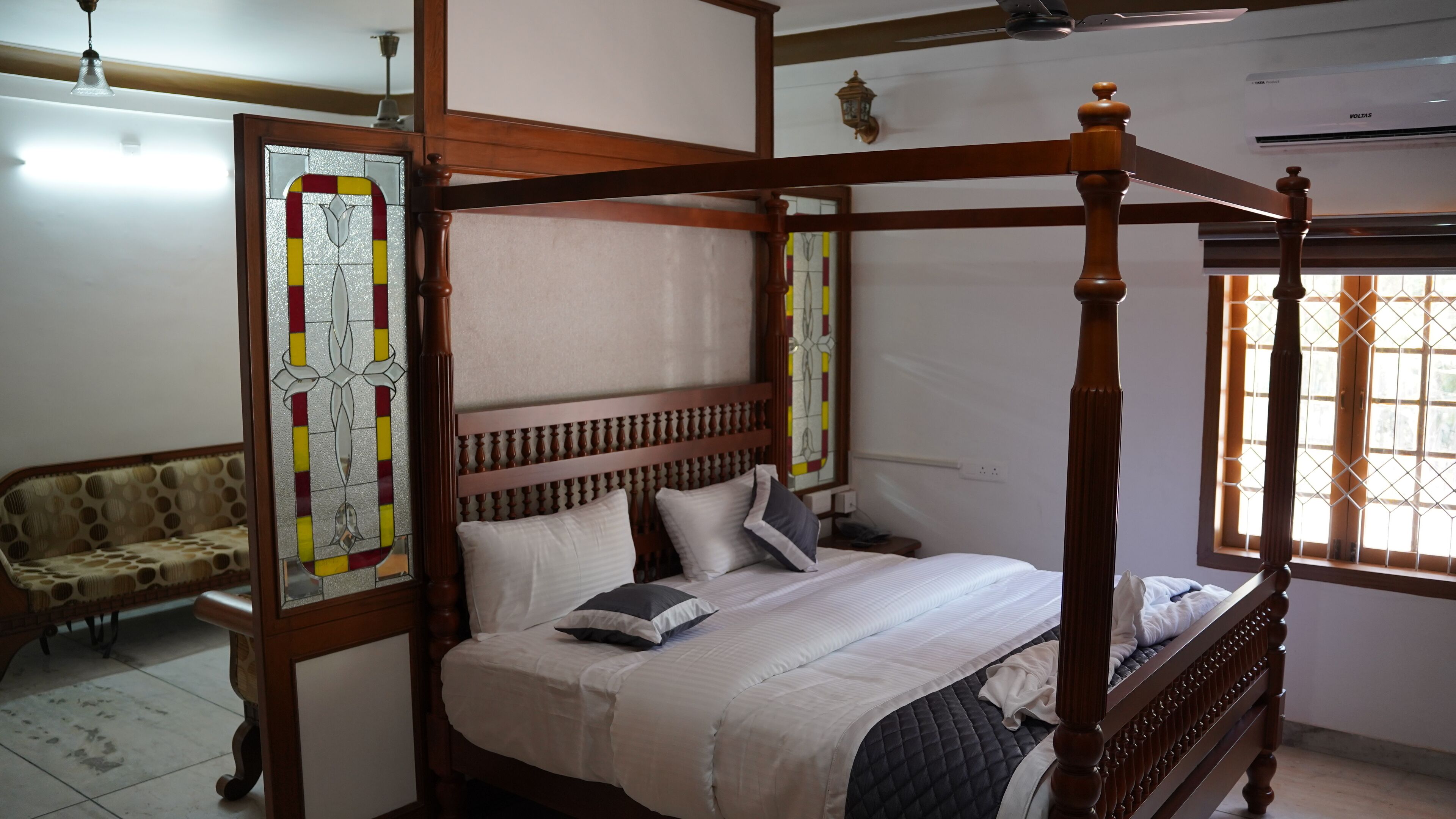 A four-poster bed with a wooden headboard, a sofa, and a stained glass window.