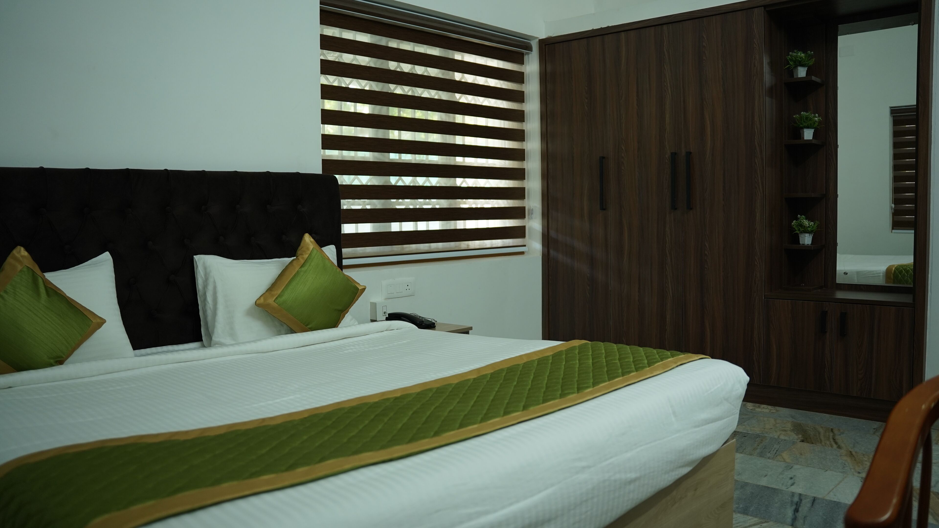 A neatly made bed with a green and white bedspread, a dark headboard, and two green pillows.