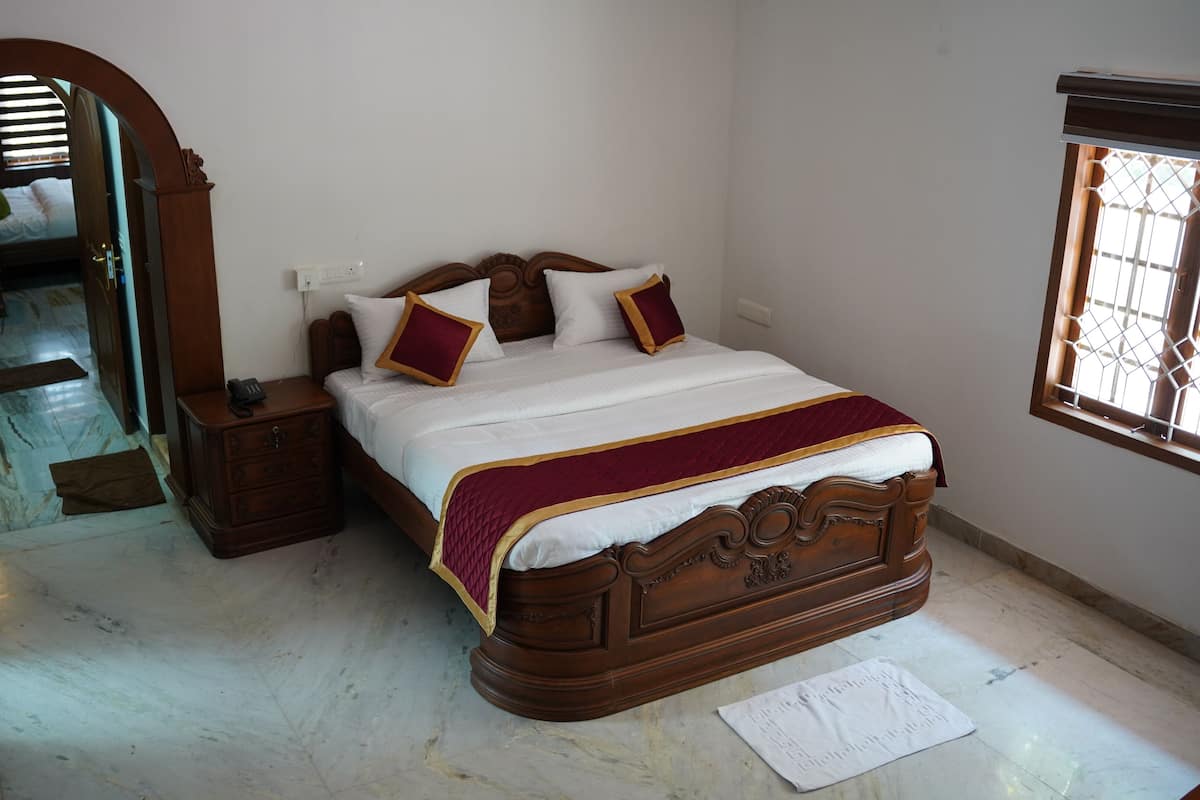 Quarto com cama de madeira, mesa de cabeceira, espelho, janela com grades e porta que dá para outro cômodo.