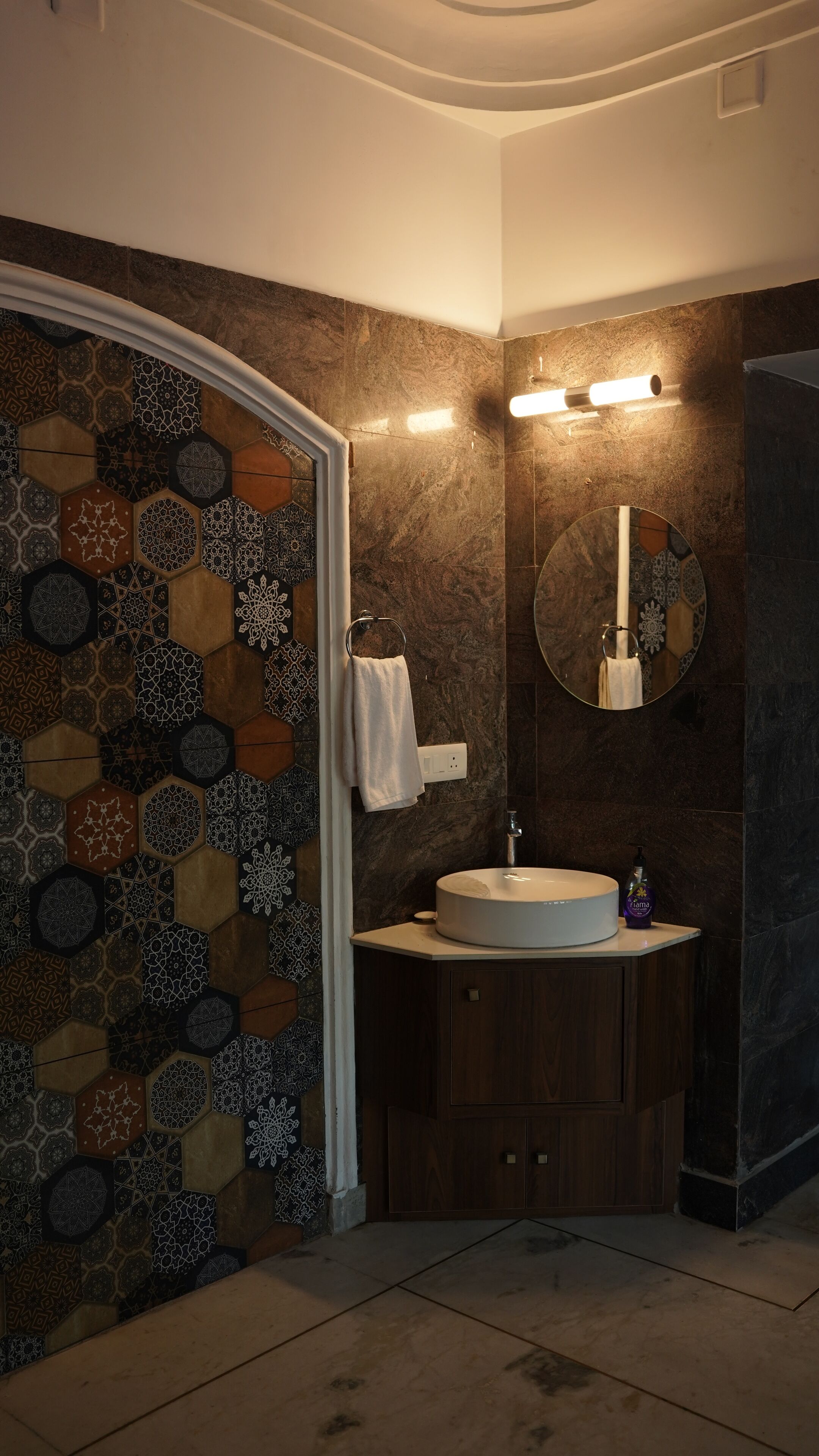 Un baño con pared de azulejos hexagonales, un espejo redondo, un lavabo y un perchero para toallas.