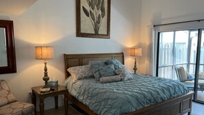 A bedroom with a large bed, two bedside tables, a chair, a window with a view, and a framed artwork on the wall. - Fabulous Naples Townhouse in Desirable Pelican Ridge Location (Naples)