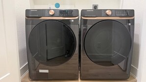 Two Samsung front-loading washing machines in a laundry room with a wooden floor. - Elegant Plush  Properties (Houston)