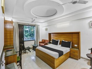 Een moderne slaapkamer met een houten bed, een plafondventilator, een raam met gordijnen en een klein tafeltje met een stoel.