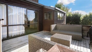 A wooden deck with wicker furniture, large sliding glass doors, and a clear sky. - Waiake Family Retreat - Auckland Holiday Home (Auckland)