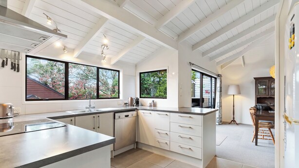 A modern kitchen with white cabinetry, a large island, and a view of the outdoors. - Waiake Family Retreat - Auckland Holiday Home (Auckland)