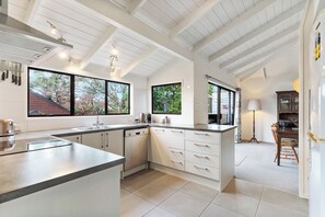 A modern kitchen with white cabinetry, a large island, and a view of the outdoors. - Waiake Family Retreat - Auckland Holiday Home (Auckland)