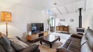 A modern living room with a flat-screen TV, leather sofas, a wooden coffee table, and a fireplace. - Waiake Family Retreat - Auckland Holiday Home (Auckland)