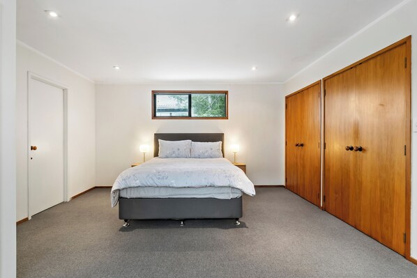 A bedroom with a bed, a wardrobe, a window, and a door. - Waiake Family Retreat - Auckland Holiday Home (Auckland)