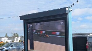 Un panneau publicitaire numérique affichant une course automobile, une table de pique-nique et une voiture garée.
