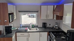 Une cuisine de taille réduite, avec des meubles blancs, une cuisinière à gaz, un évier et une fenêtre donnant sur l’extérieur.