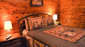 A wooden cabin-style room with a bed, two bedside lamps, and a framed picture on the wall.