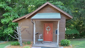 A wooden cabin with a red door, a porch with a bench, and a wreath on the door.