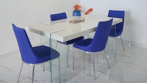 Een moderne eetruimte met een witte tafel, blauwe stoelen en een tafel met glazen blad.