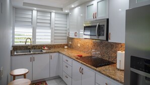 Een moderne keuken met witte kasten, granieten aanrechtbladen, een roestvrijstalen koelkast en een ingebouwde magnetron.