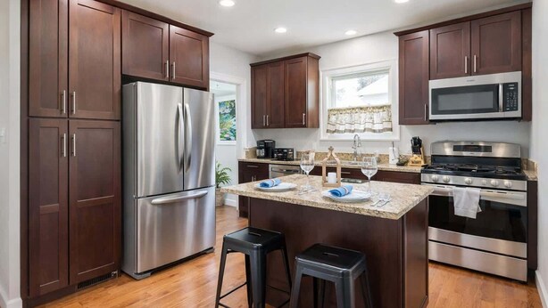 Una cocina moderna con armarios de madera oscura, electrodomésticos de acero inoxidable, encimera de granito y una pequeña isla con taburetes.