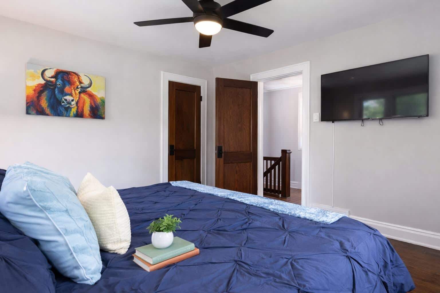 A bedroom with a bed, a ceiling fan, a TV, and a door leading to another room.
