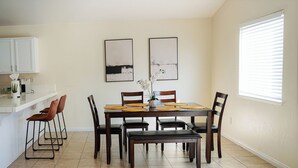 A dining area with a table set for six, surrounded by chairs, and a kitchen area with white cabinets and a countertop. - Spacious Home Right off 99 Fwy (Bakersfield)