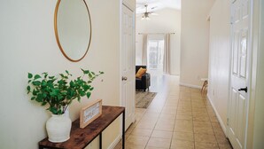A hallway with a white door, a wooden console table with a potted plant, and a mirror on the wall. - Spacious Home Right off 99 Fwy (Bakersfield)
