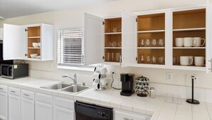 A modern kitchen with white cabinets, a dishwasher, a coffee maker, and a wine rack. - Spacious Home Right off 99 Fwy (Bakersfield)