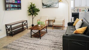 A living room with a wooden coffee table, two chairs, a sofa, a potted plant, a painting, and a mounted TV displaying streaming services. - Spacious Home Right off 99 Fwy (Bakersfield)