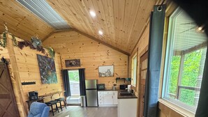 Een gezellig chaletinterieur met houten details, een bank, een eettafel, een keukenhoek en een groot raam.