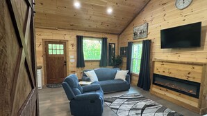 Een gezellige kamer met houten wanden, een open haard, een bank en een televisie.