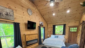 Een gezellig vakantiehuisje met houten inrichting, een bed, een bank, een kleine tafel en een open haard.