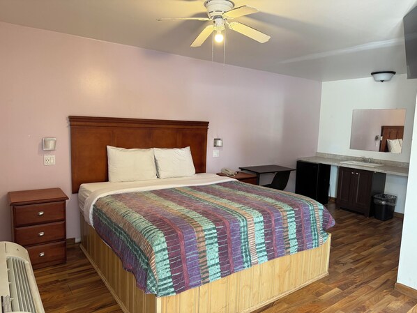A bedroom with a wooden headboard, a bed with a colorful quilt, a desk, a chair, a small dresser, a mirror, and a ceiling fan. - Pleasant Hill Motel (Lockport)