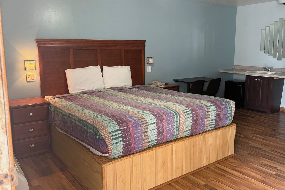 A bedroom with a wooden bed, a desk, and a small kitchenette.