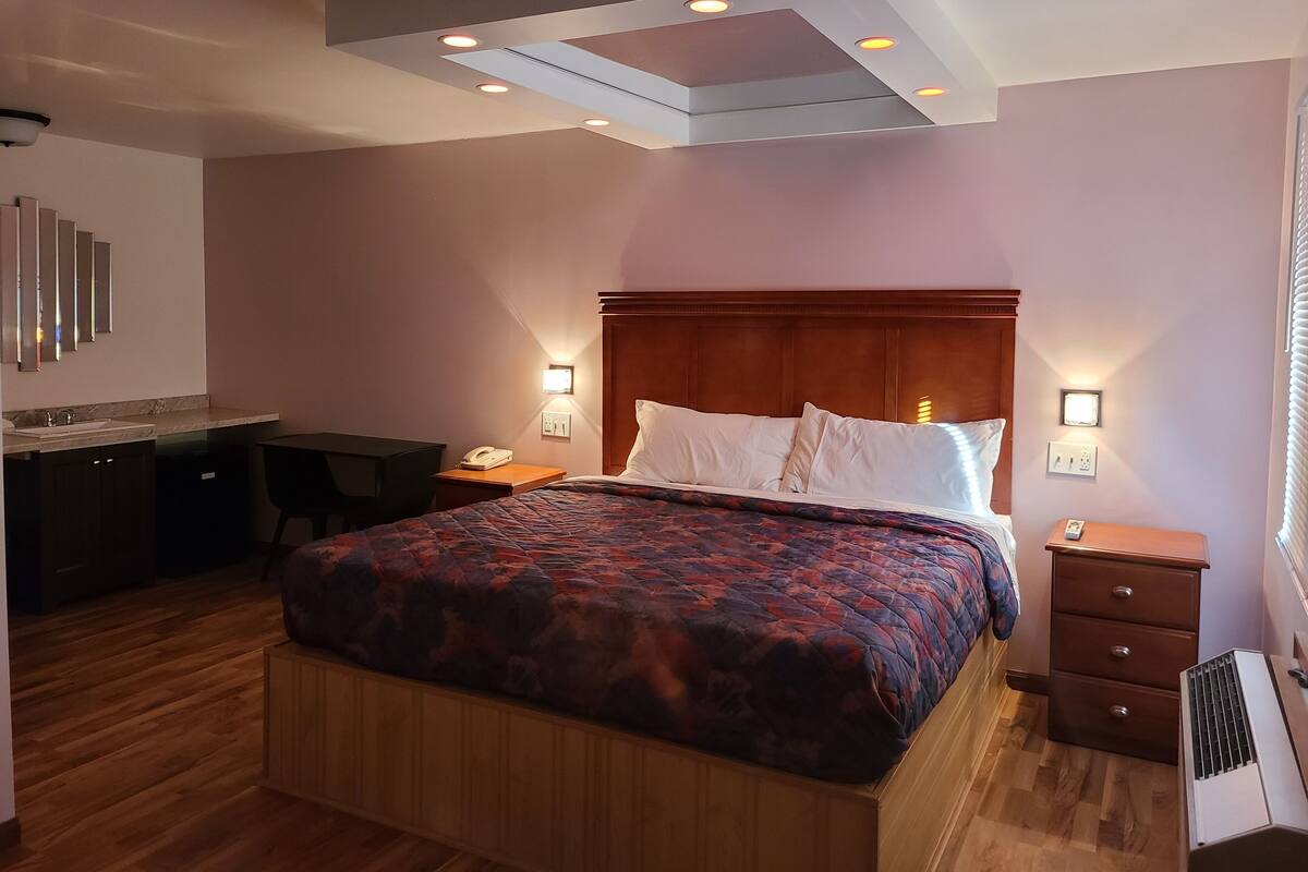 A hotel room with a large bed, a desk, and a chair. There are two bedside tables with lamps.