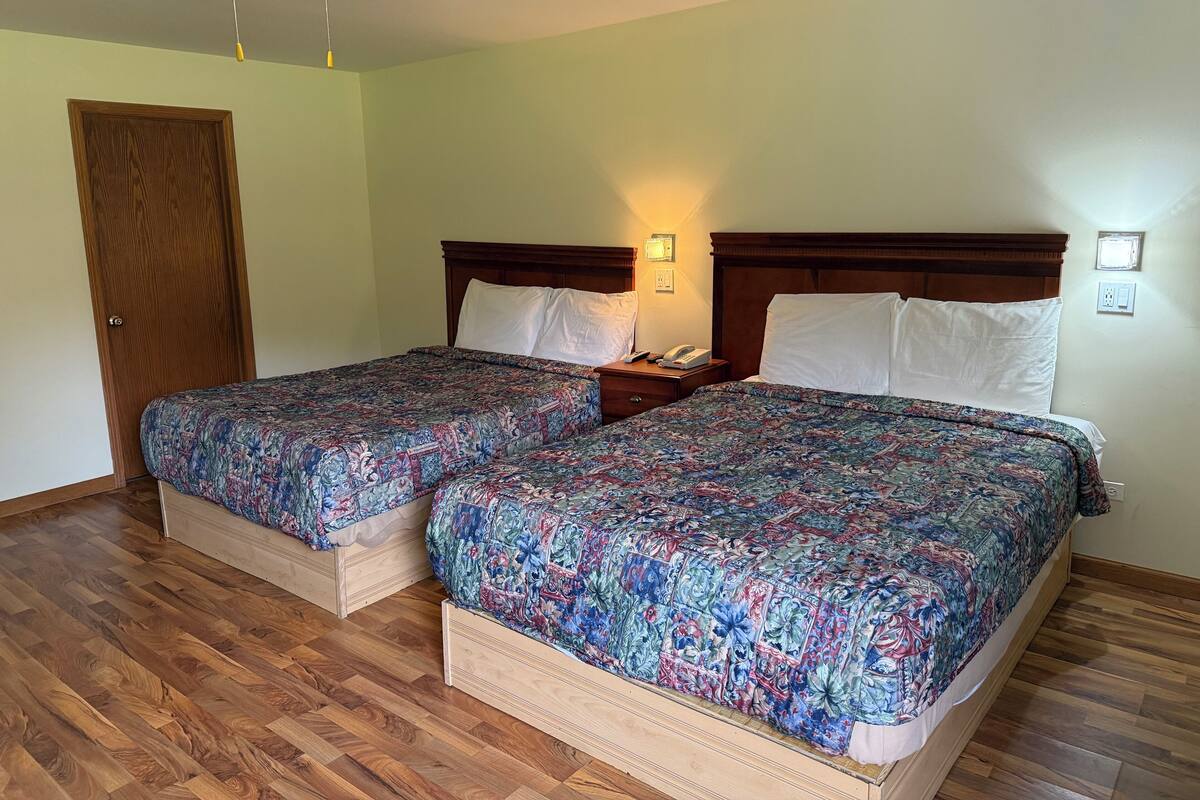 A hotel room with two beds, wooden flooring, a ceiling fan, and a door.