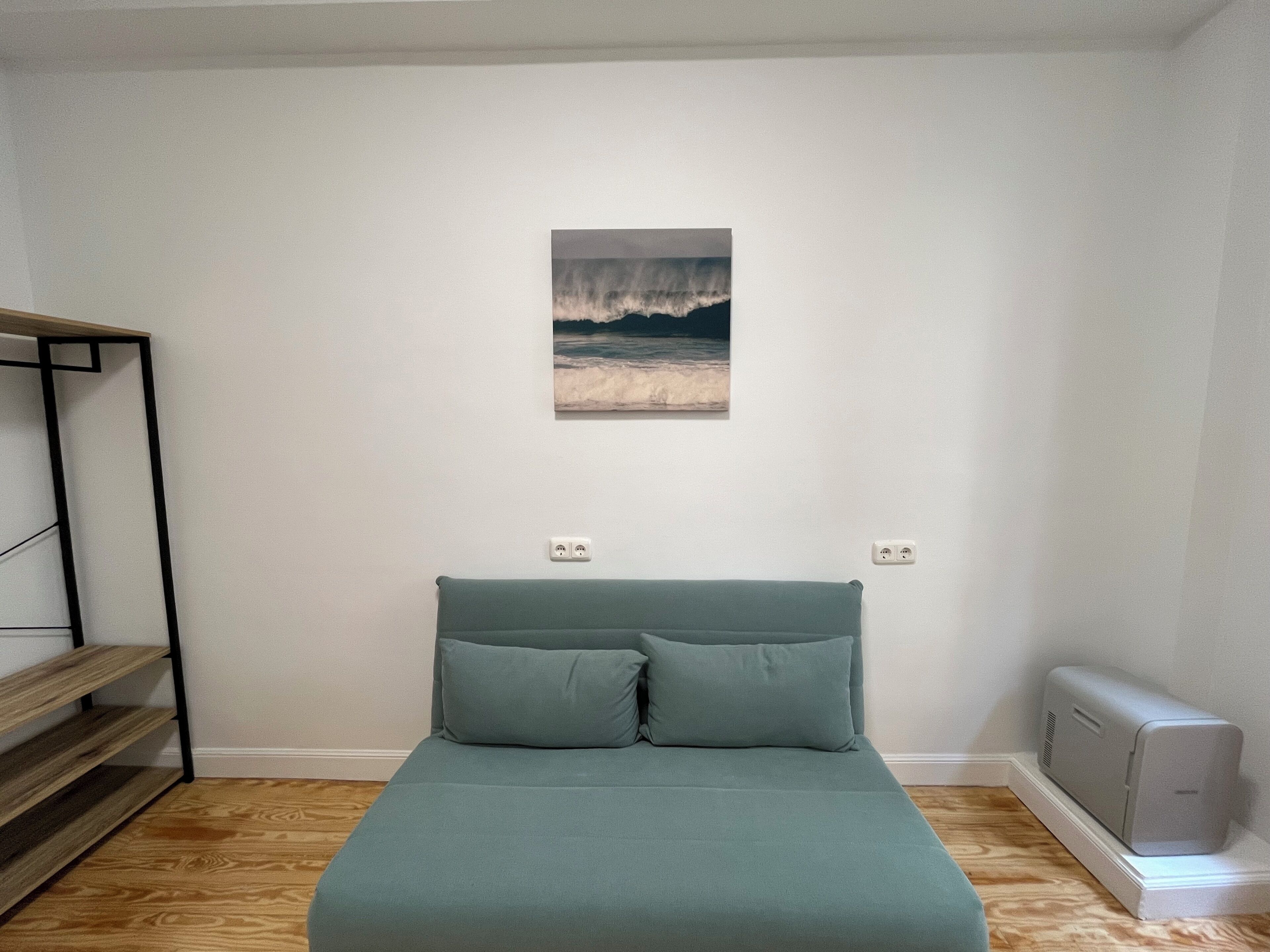 Un dormitorio con cama, estante, cuadro y radiador.