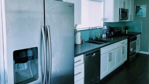 A modern kitchen with stainless steel appliances, white cabinets, a black countertop, and a window with blinds. - perfect getaway. sf view. free parking on site (Oakland)