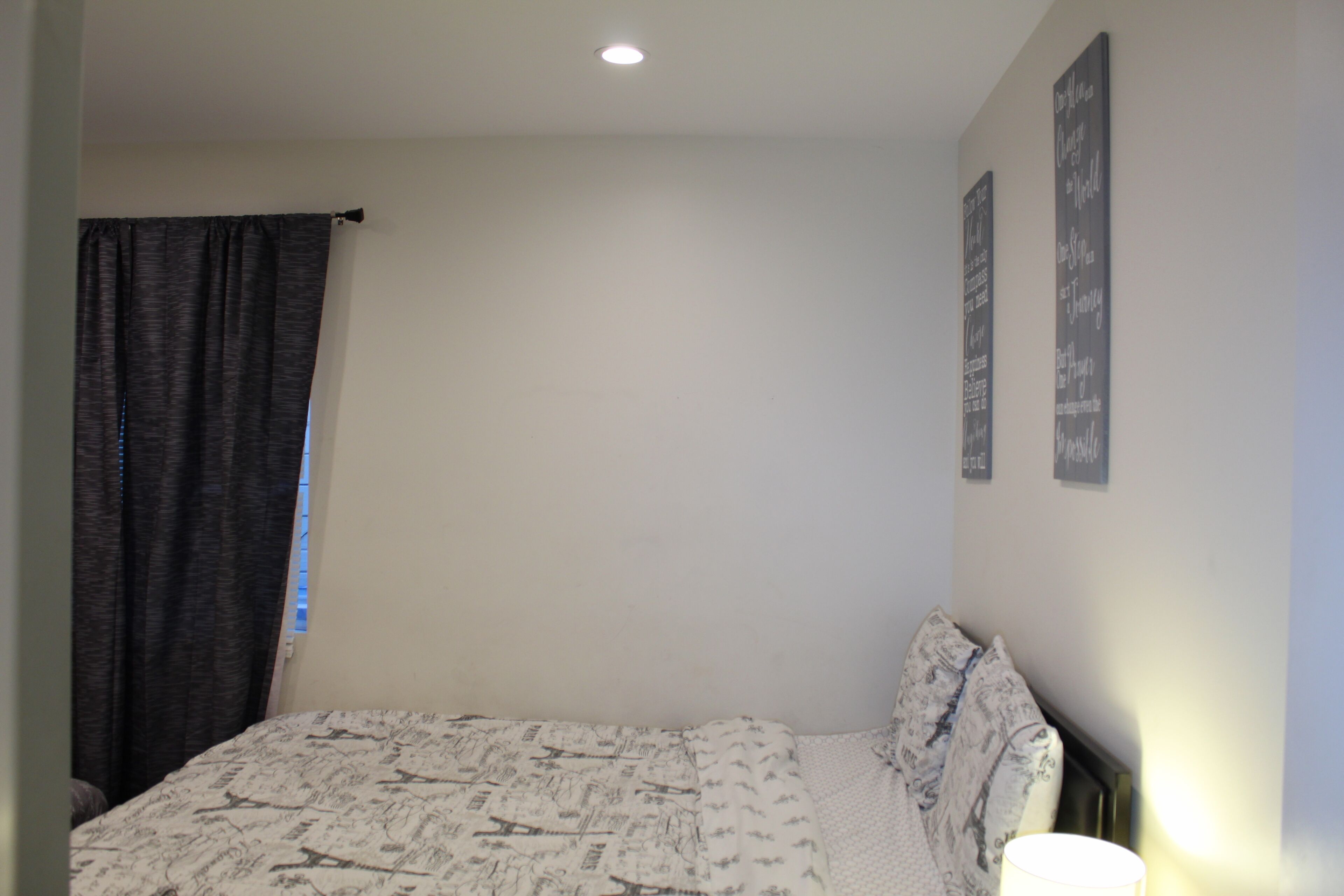 Une chambre à coucher avec un lit, une fenêtre avec des rideaux et deux panneaux décoratifs fixés au mur.