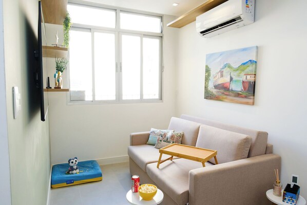 A living room with a sofa, a small table, a television, a painting, and a window. - Copacabana refuge, comfort 190m from the beach. (Copacabana Rio de Janeiro)