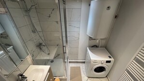 A modern bathroom with a glass-enclosed shower, a built-in washing machine, and a large white water heater. - Large American Studio (Toulon)