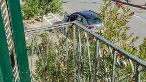 Ein Balkon mit Blick auf eine Straße, ein geparktes Auto und eine mit Pflanzen bepflanzte Umzäunung.