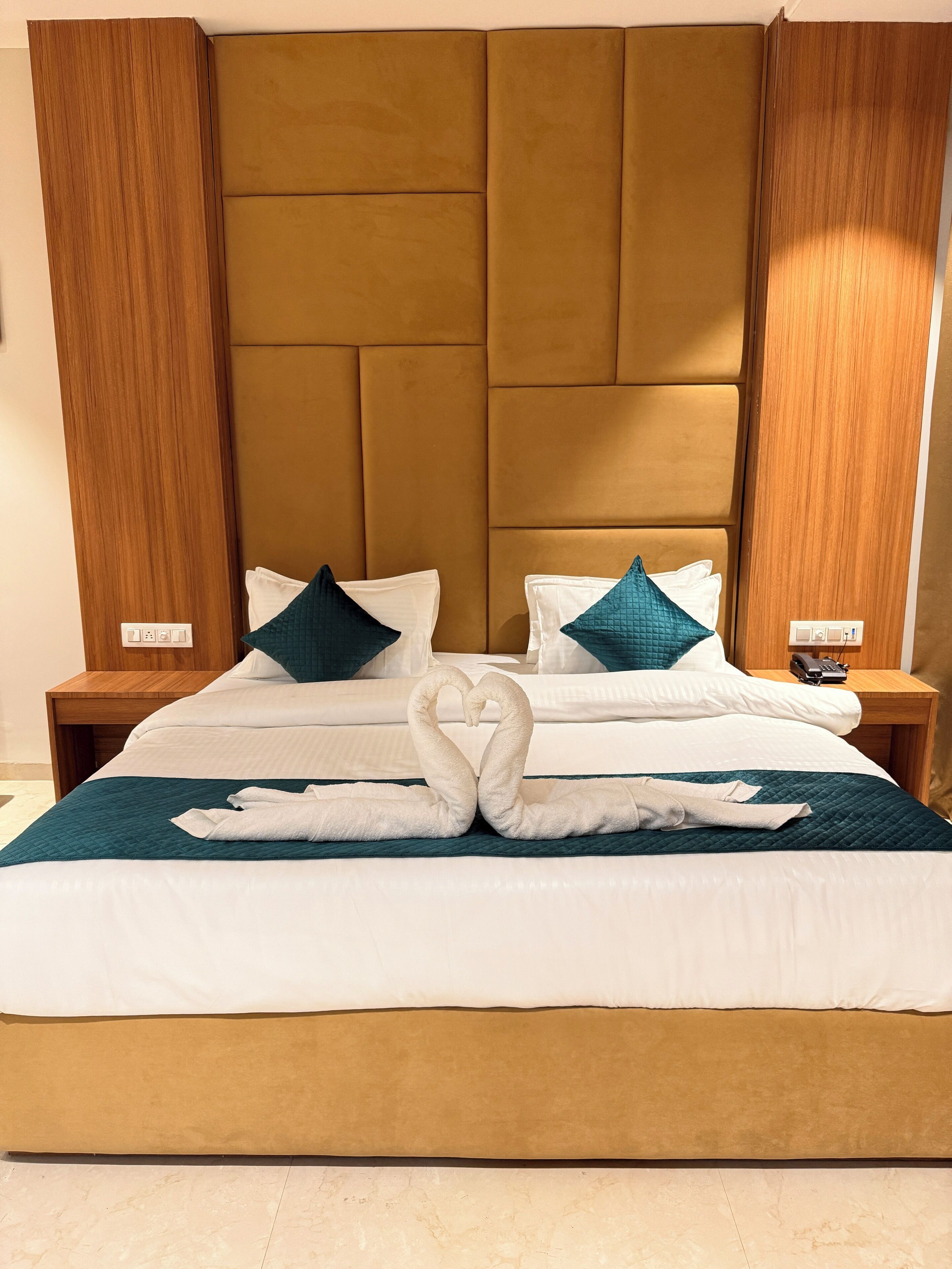 Een hotelkamer met een groot bed, een houten hoofdeinde en een nachtkastje met een telefoon.