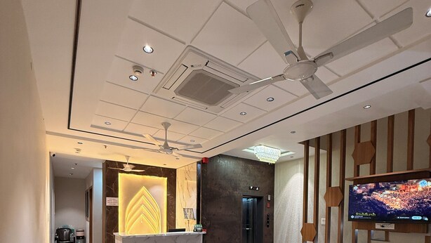 A modern lobby with a reception desk, seating area, ceiling fans, and a television screen. - Hotel Akaay (Ujjain)